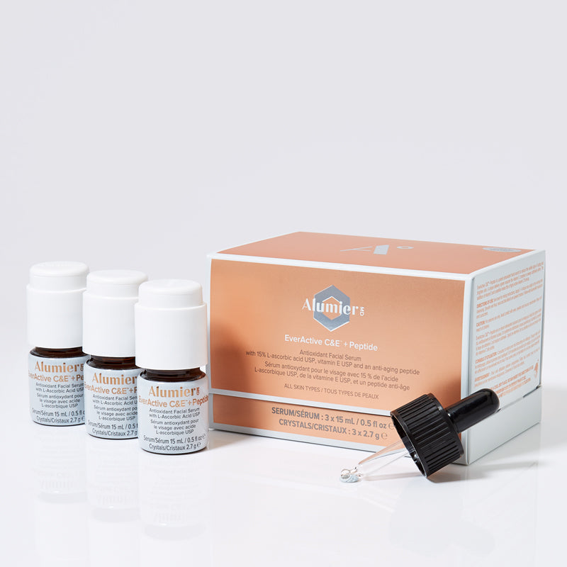 Three small vials labeled "AlumierMD EverActive C&E + Peptide Serum" stand next to a salmon-colored box with the same branding. A dropper rests on the box. Text:
AlumierMD
EverActive C&E + Peptide
Antioxidant Facial Serum
with 15% L-Ascorbic acid USP, Vitamin E, and an anti-aging peptide
with all skin types
Serum: 3 x 15 mL /0.51 fl. oz.
Crystals: 3 x 2.7 g