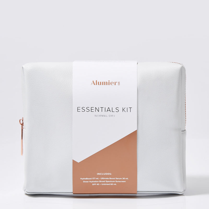 A white pouch with a vertical tag labeled "AlumierMD ESSENTIALS KIT NORMAL/DRY," set against a plain background. Text includes, "INCLUDES: HydraBoost, Ultimatte Boost Serum 30 ml, Sheer Hydration Broad Spectrum Sunscreen SPF 40-Untinted 60 ml."