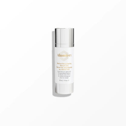 A white bottle labeled "AlumierMD Retinol Resurfacing Serum 0.5" with a metallic cap stands upright on a smooth, light grey surface in a minimalistic setting. Text includes: "Serum de resurfaçage au rétinol 0.5%, Facial Serum with 0.5% Encapsulated Retinol, 30 mL / 1 fl oz."