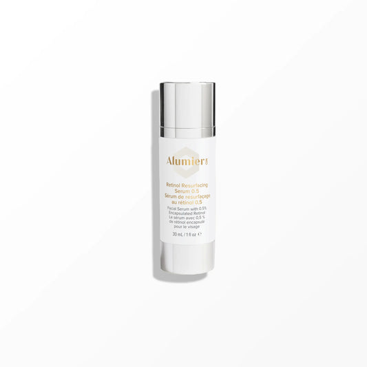 A white bottle labeled "AlumierMD Retinol Resurfacing Serum 0.5" with a metallic cap stands upright on a smooth, light grey surface in a minimalistic setting. Text includes: "Serum de resurfaçage au rétinol 0.5%, Facial Serum with 0.5% Encapsulated Retinol, 30 mL / 1 fl oz."