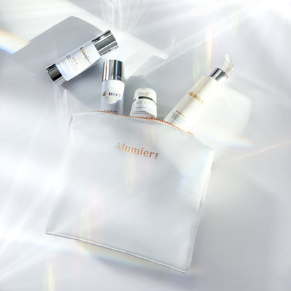 A white pouch labeled "Alumier MD" contains five skincare products with metallic caps, all positioned in a softly lit, glossy environment with reflective surfaces.