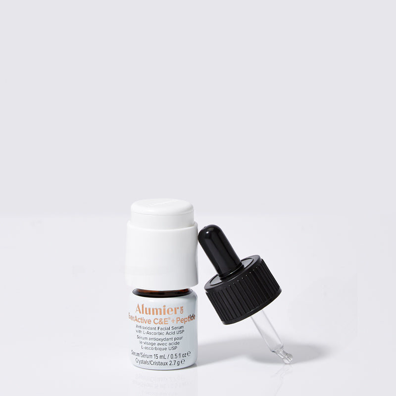 A small brown serum bottle labeled "AlumierMD EverActive C&E + Peptide" with a white cap, next to a black dropper lying on a white surface. Text includes "An antioxidant serum... 15 mL/0.5 fl oz".