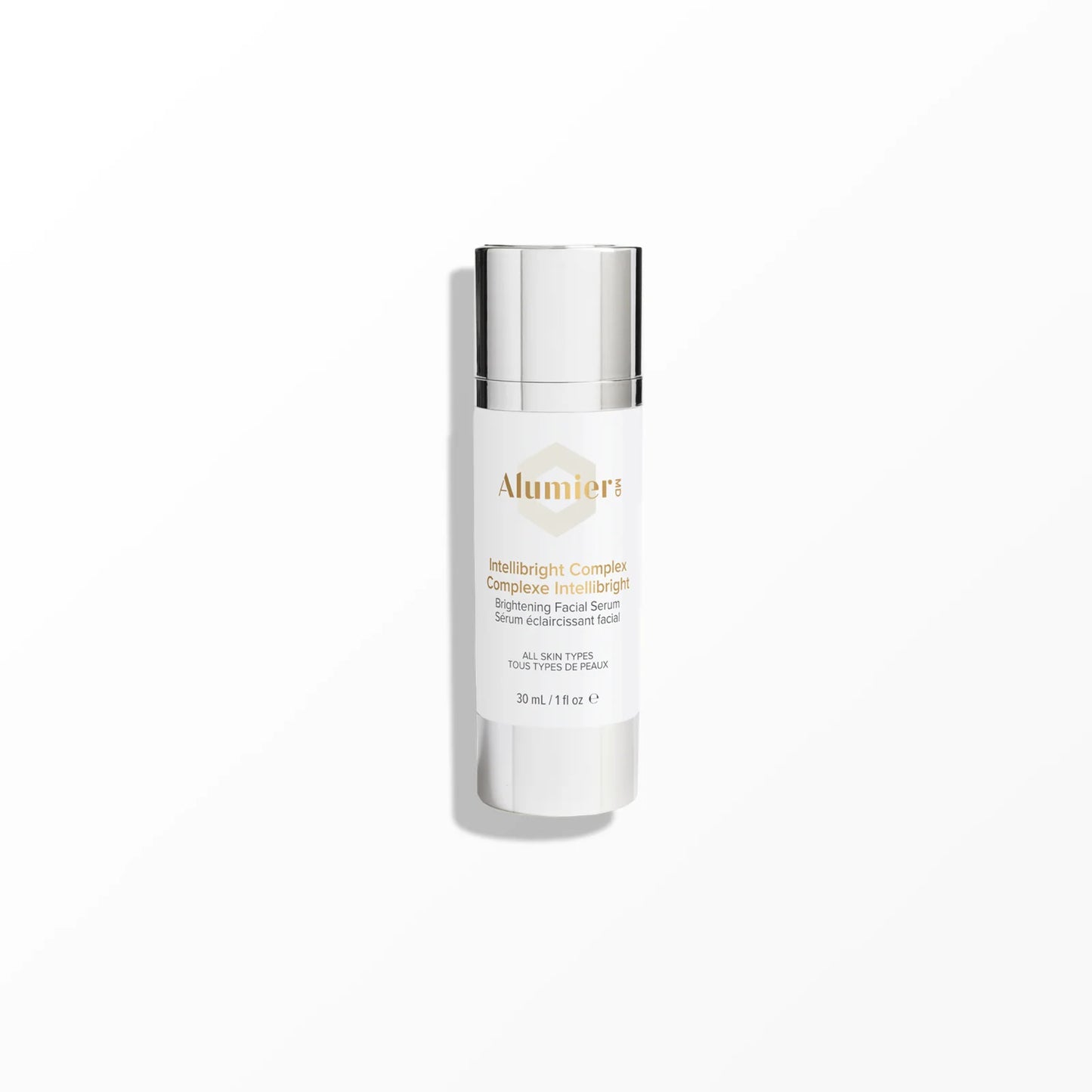 A white cylindrical bottle with a silver cap labelled "Alumier MD Intellibright Complex Brightening Facial Serum, All Skin Types, 30mL / 1.1 fl oz" stands on a smooth, light-grey surface against a plain background.