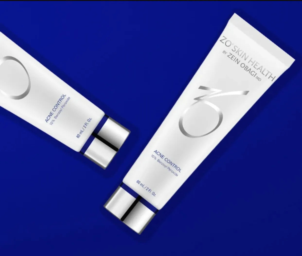 Two white tubes of "ZO SKIN HEALTH by ZEIN OBAGI MD Acne Control, 10% Benzoyl Peroxide," lie on a vibrant blue surface. Each tube contains 60 ml / 2 FL. Oz.