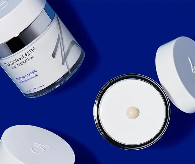 A jar of "ZO Skin Health" Renewal Crème by Zein Obagi MD is open, displaying the cream inside. The jar and lid lay on a blue surface.