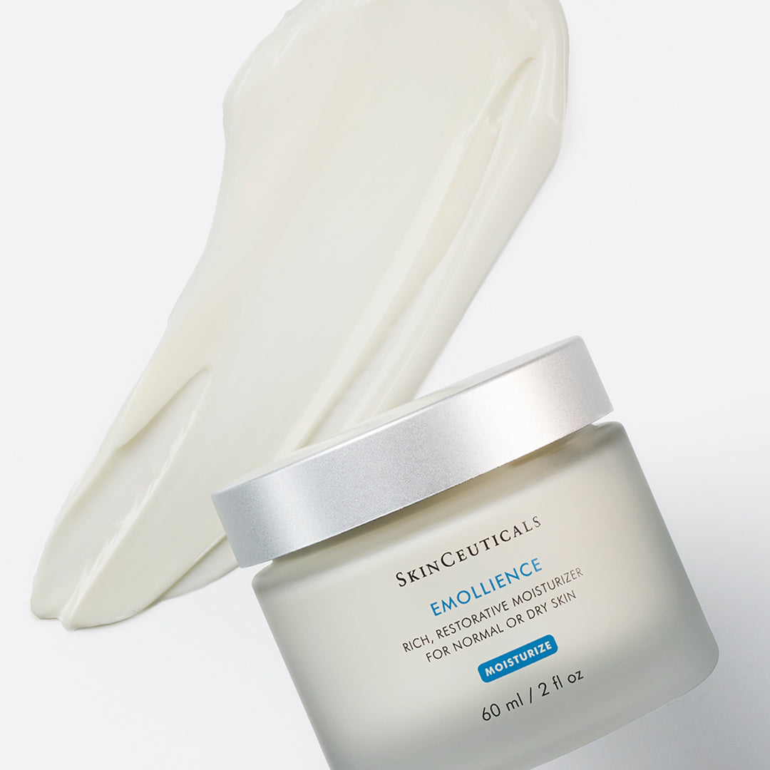 A jar of SkinCeuticals Emollience moisturizer rests in front of a smooth, spread layer of the cream. Text on the jar reads: "SkinCeuticals Emollience Rich, Restorative Moisturizer for Normal or Dry Skin. Moisturizer. 60 ml / 2 fl oz."