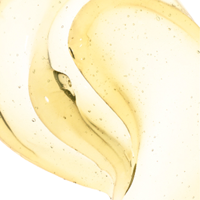 Translucent, viscous yellow liquid with bubbles, flowing in overlapping, wavy layers against a white background.