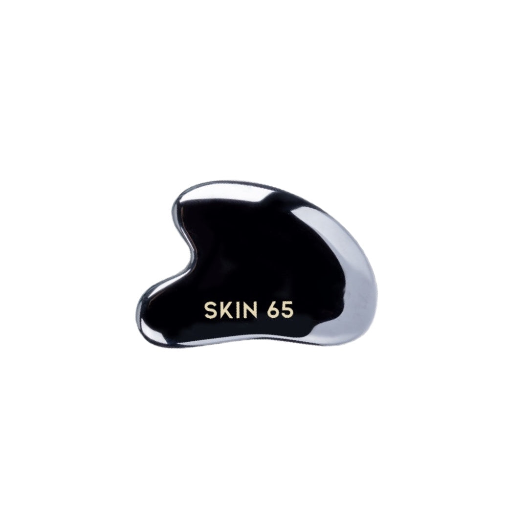 A black, ergonomically-shaped skin care tool with smooth curves, inscribed with "SKIN 65" in gold text, rests against a plain white background.