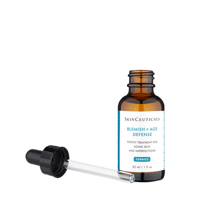 A brown glass bottle labeled "SkinCeuticals Blemish + Age Defense," positioned upright, alongside a dropper with a black cap lying down. Text on the label: "Potent treatment for aging skin and imperfections. 30 ml / 1 fl oz."